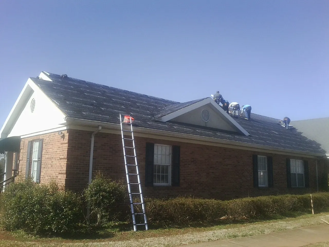 Crew tearing shingles off a brick ranch roof with a ladder set — Emergency Roof Repair work by our crew in Pine Beach
