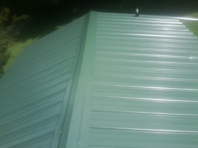 New green metal panels meeting at the ridge of a roof — Flat Roof Repair work by our crew in Pine Beach