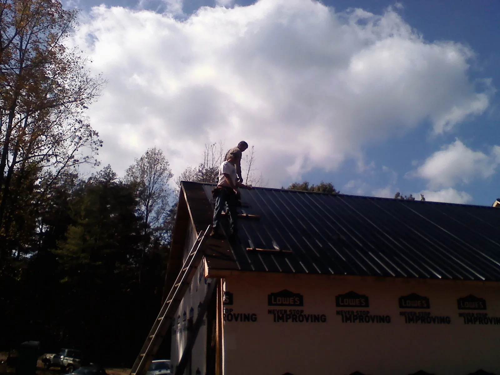 Roofer fastening dark metal panels high against a cloudy sky, from a Roof Inspection job in Pine Beach